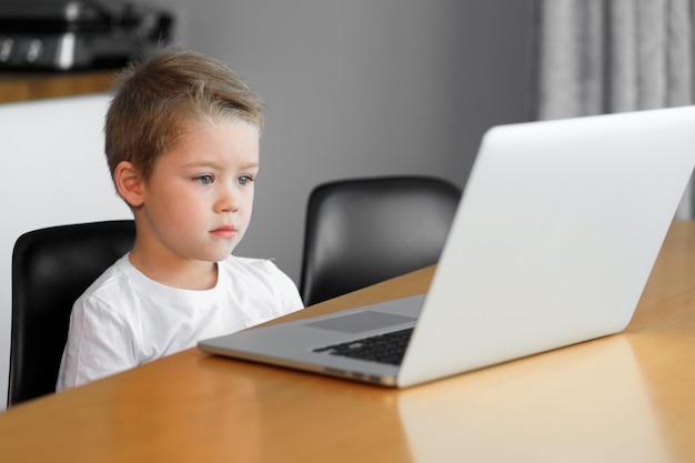 Un muchacho joven que usa una computadora portátil que se sienta encima de una tabla en casa.