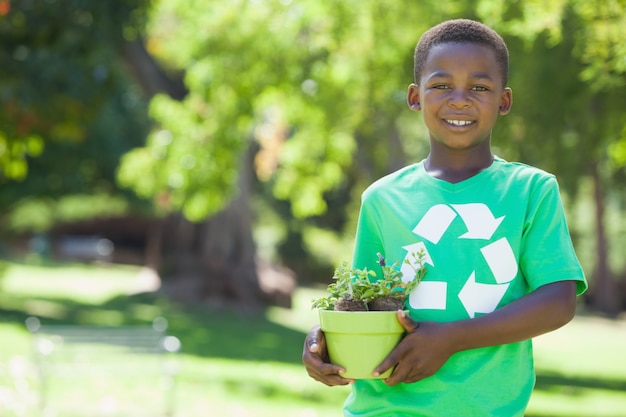 Muchacho joven en el reciclaje de la camiseta que sostiene la planta en conserva