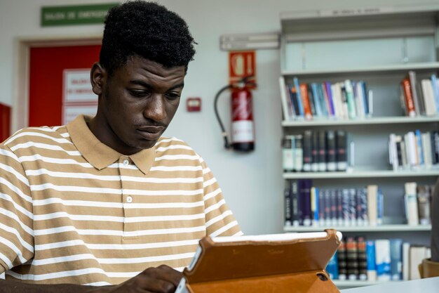 Muchacho negro joven que usa una tableta en una biblioteca