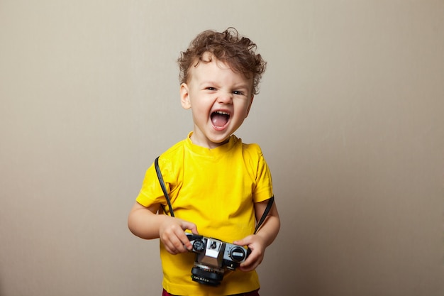 El muchacho del niño 2 años que lleva la ropa amarilla sostiene la cámara aislada, retrato del estudio de los niños.