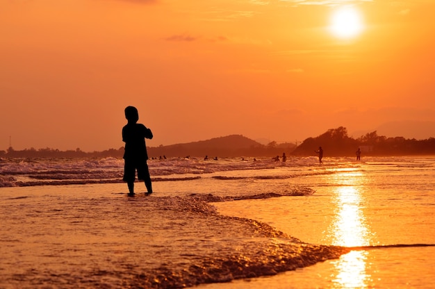 Muchacho de silueta de pie en la playa al atardecer