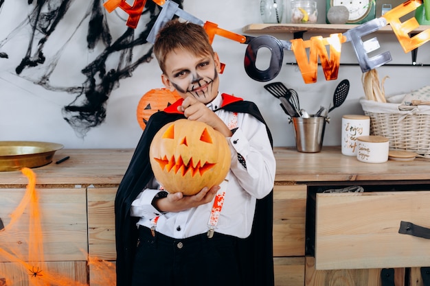 Foto muchacho sonriente que se coloca en el vestido de mascarada que sostiene una calabaza