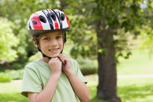 Muchacho sonriente que desgasta el casco de la bicicleta en el parque