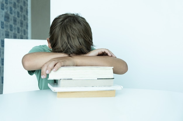 El muchacho triste con el libro hace la tarea escolar. De vuelta a la escuela. Colegial infeliz con libros de texto. La educación a distancia.