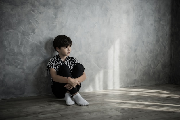 Muchacho triste sentado pensando sentado en el piso de la habitación contra la pared de la casa.