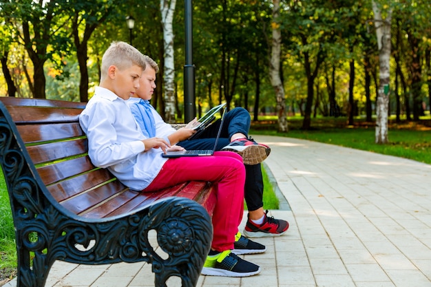 Muchachos adolescentes en el banco del parque con ordenador portátil y tableta digital.