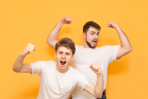 los muchachos con camisetas blancas se regocijan con las manos levantadas en amarillo