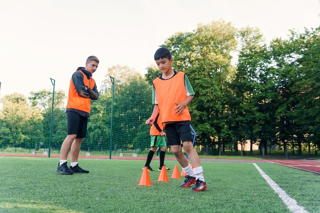 Muchachos motivados con chalecos naranjas corriendo entre los conos de plástico durante el entrenamiento de fútbol en el estadio.