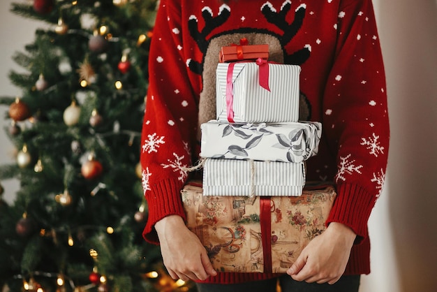 Muchas cajas de regalo de Navidad en las manos en el hermoso árbol de Navidad dorado con luces en la sala festiva vacaciones de invierno momentos atmosféricos temporadas saludos Feliz Navidad