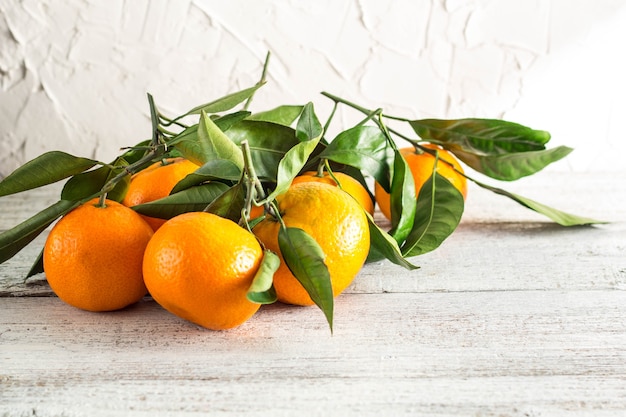 Muchas mandarinas naranjas con hojas verdes sobre fondo blanco de madera