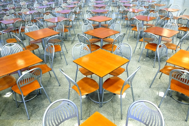 Muchas mesas cuadradas marrones y sillas metálicas en una sala de café vacía dentro de un edificio moderno