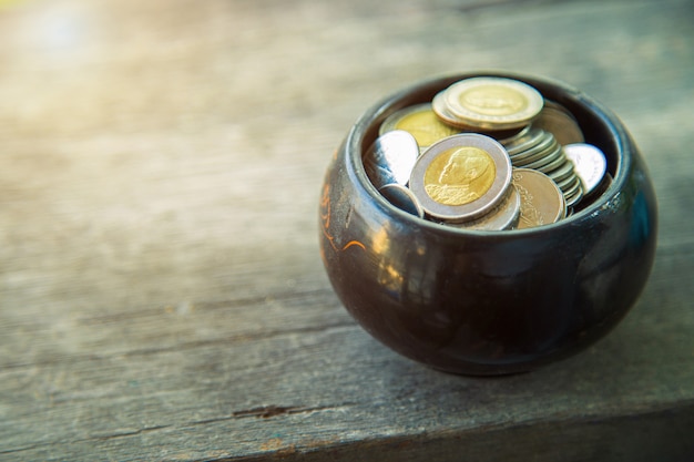 Muchas monedas en bown tazón de madera en mesa de madera