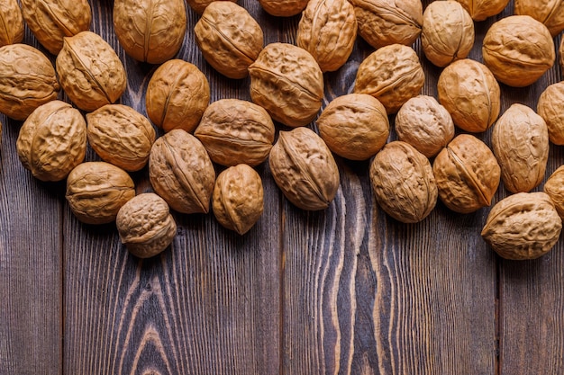 Muchas nueces con cáscaras esparcidas al azar sobre una superficie de madera marrón con espacio para copiar en la parte inferior de la imagen