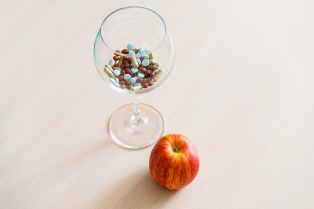 Muchas pastillas de diferentes colores en una copa de vino y manzana roja fresca