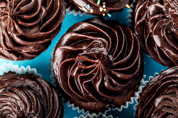 Muchas pequeñas magdalenas lindas del chocolate para el partido o el cumpleaños en fondo azul. Vista superior.