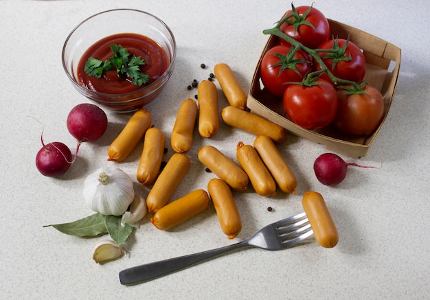 Foto muchas salchichas pequeñas especias tomates y tenedor sobre un fondo de mármol