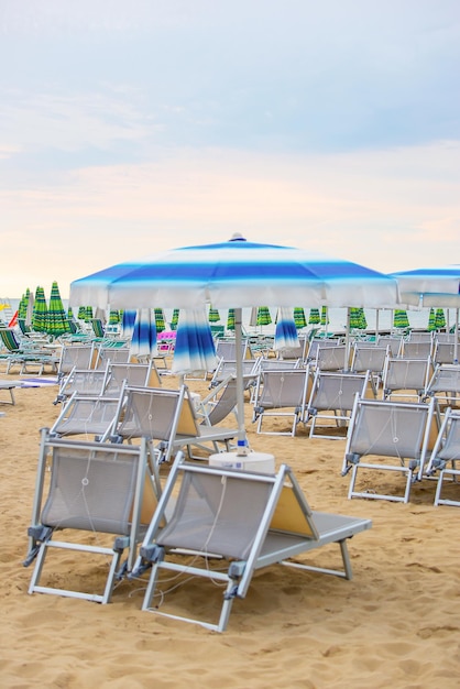 muchas sombrillas cerradas y tumbonas en una playa vacía Concepto de inicio o fin de temporada