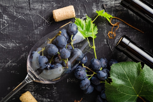 Muchas uvas en copa de vino. Botellas de vino, racimos de uva con hojas y vides corchos de vino en la oscuridad