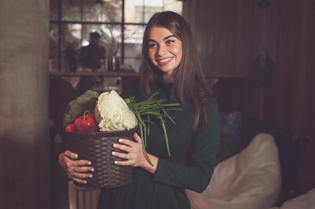 Con muchas verduras diferentes en la canasta, una mujer hermosa está de pie