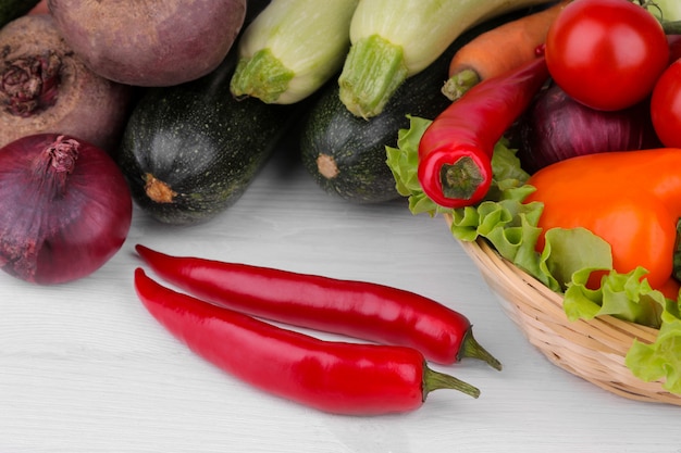 Muchas verduras diferentes en la canasta sobre una superficie de madera blanca