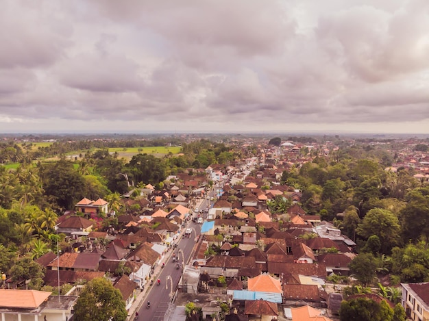 Muchas villas con techos de tejas de color marrón anaranjado entre árboles tropicales en el fondo del cielo en Ubud en Bali Sun brilla sobre ellos Foto horizontal aérea