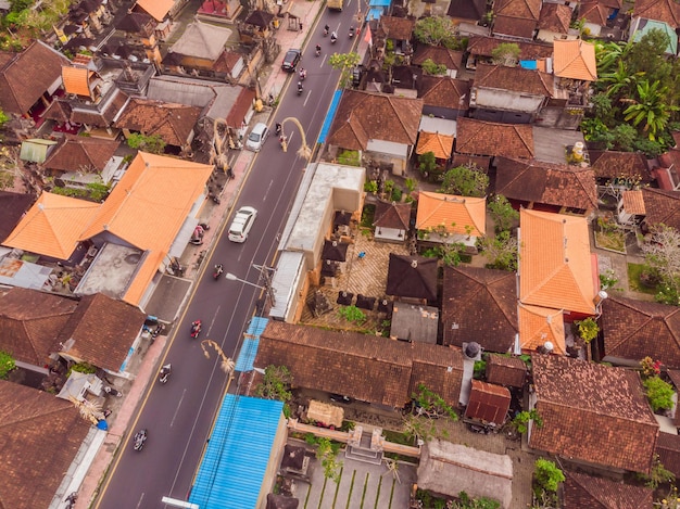 Muchas villas con techos de tejas de color marrón anaranjado entre árboles tropicales en el fondo del cielo en Ubud en Bali Sun brilla sobre ellos Foto horizontal aérea