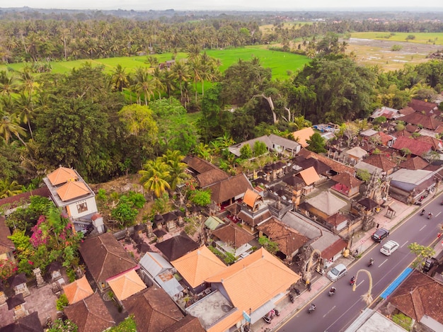 Muchas villas con techos de tejas de color marrón anaranjado entre árboles tropicales en el fondo del cielo en Ubud en Bali Sun brilla sobre ellos Foto horizontal aérea