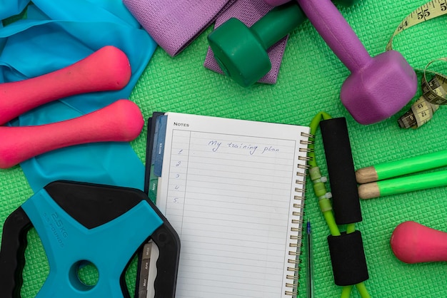 muchos accesorios deportivos diferentes en una alfombra deportiva y un cuaderno para escribir. El concepto de accesorios deportivos.