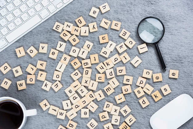 Muchos bloques de madera del alfabeto con el teclado; ratón; Lupa y taza de café en el escritorio