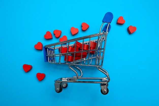 Muchos corazones rojos en un mini carrito de supermercado sobre fondo azul Concepto de compras en línea