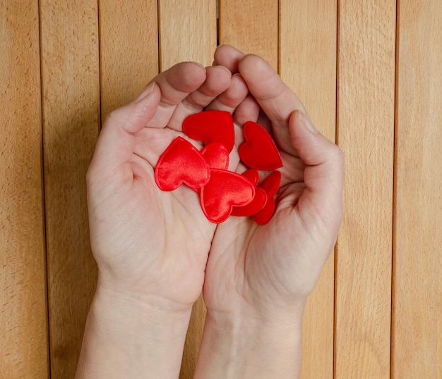 Muchos corazones rojos en las palmas de las mujeres Fondo de madera