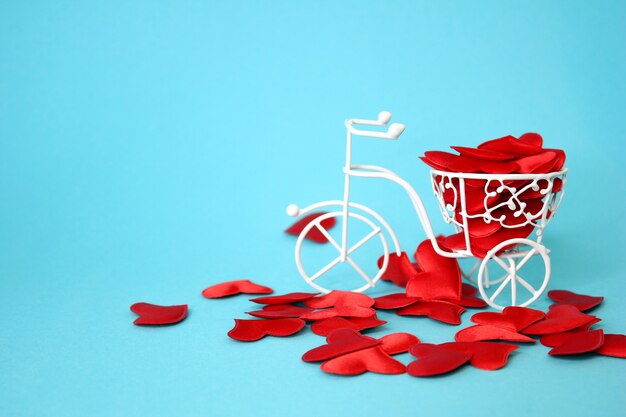 Muchos corazones rojos son impulsados por una bicicleta decorativa blanca hecha de alambre. Fondo azul. Concepto de San Valentín. La idea del amor.