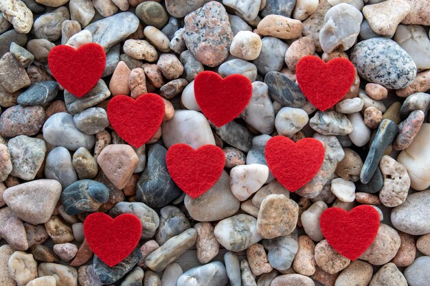Muchos corazones de tela roja en el río piedras de guijarros