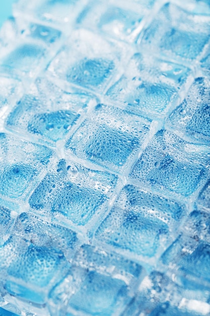 Muchos cubitos de hielo helados y refrescantes con gotas sobre un fondo azul Bebidas refrescantes cuando hace calor