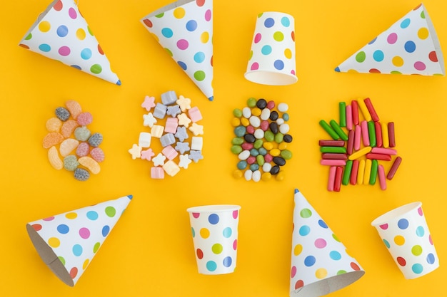 Muchos dulces diferentes dulces y sombrero de cumpleaños sobre fondo amarillo