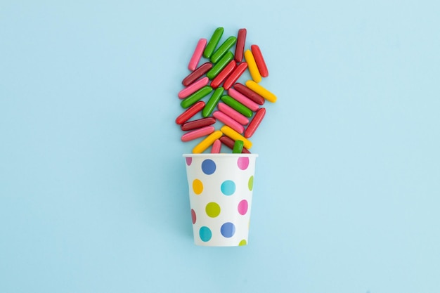 Muchos dulces diferentes en vaso de papel sobre fondo azul.