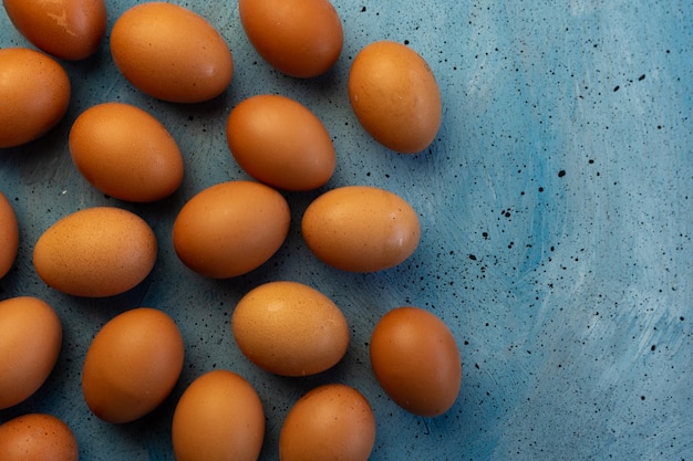 muchos huevos de gallina marrón sobre una superficie azul