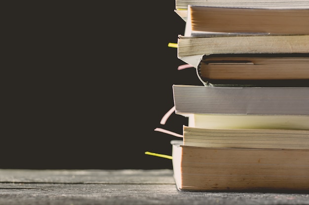 Muchos libros están apilados en una mesa de madera en una habitación oscura con luces brillantes.