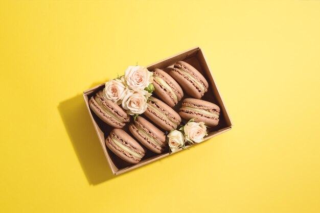 Muchos macarons de chocolate en caja artesanal con rosas en el fondo amarillo