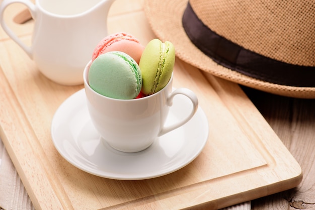 Muchos macarons coloridos franceses en un piso arbolado, macarons en una taza