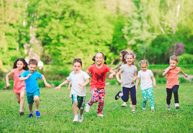 Muchos niños, niños y niñas diferentes corriendo en el parque en un día soleado de verano en ropa casual