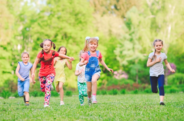 Muchos niños, niños y niñas diferentes corriendo en el parque en un día soleado de verano en ropa casual