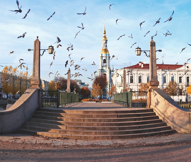 Muchos pájaros sobre el antiguo puente sobre el canal y la iglesia azul en el parque de otoño