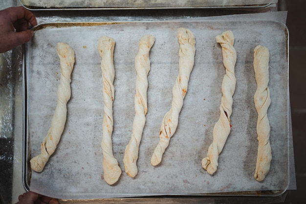 Muchos palitos de pan hechos a mano rellenos en una bandeja de metal descansando antes de entrar al horno