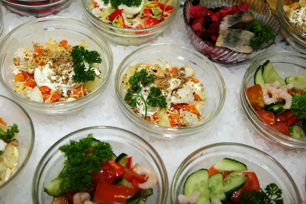 Muchos platos de vidrio con una variedad de ensaladas están sobre hielo