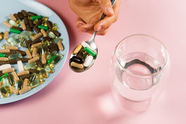 Muchos suplementos dietéticos tabletas vaso de agua y cuchara para la ingesta diaria de pastillas sobre fondo rosa Conjunto de pastillas de zinc antioxidantes del envejecimiento lecitina y adaptógeno