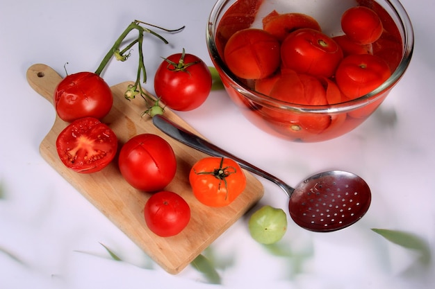 muchos tomates blanqueados en un recipiente con agua, listos para pelar