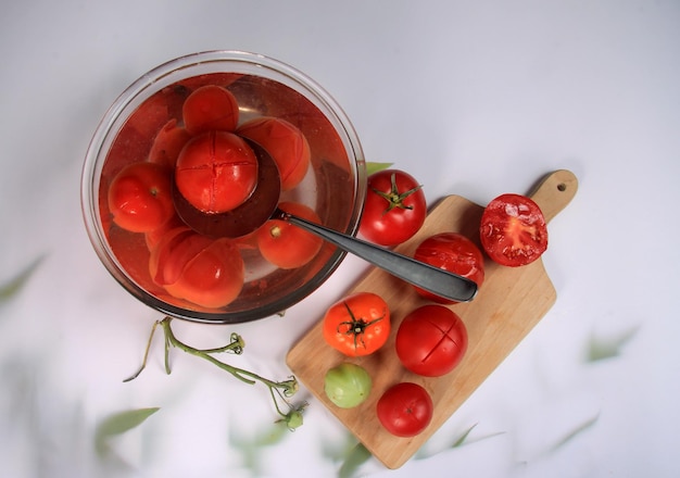 muchos tomates blanqueados en un recipiente con agua, listos para pelar