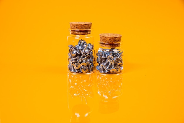 Muchos tornillos autorroscantes de metal hechos de acero en un vaso en un tarro de cubo tornillo autorroscante para metal para tornillos autorroscantes cromados de hierro sobre un fondo amarillo anaranjado