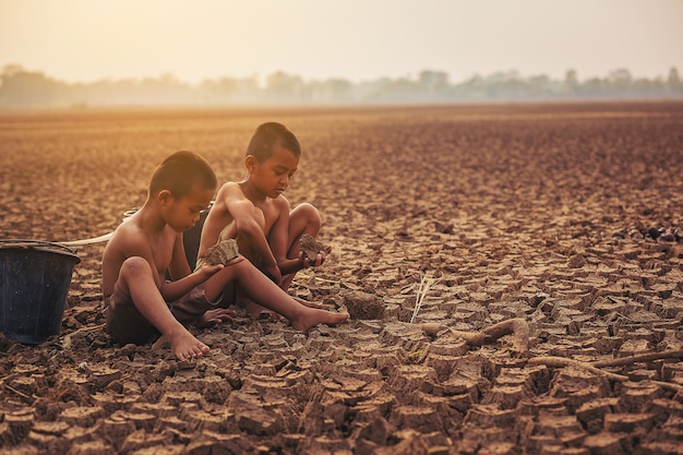 Mudança climática Dois meninos asiáticos caminhando em busca de água em solo seco e no pôr do sol Conservação do meio ambiente e fim do aquecimento global conceito